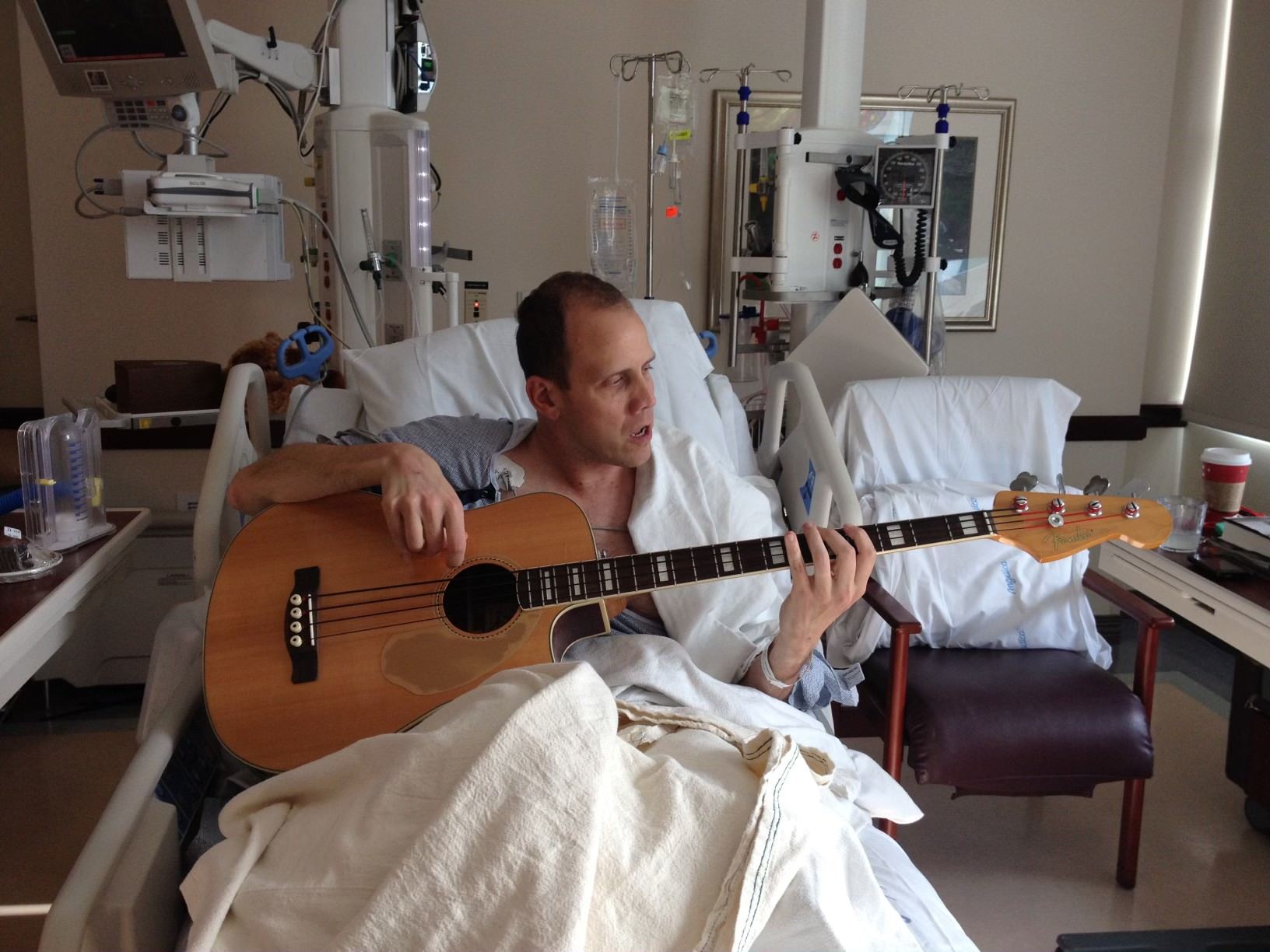 Doug playing bass guitar in a hospital bed.